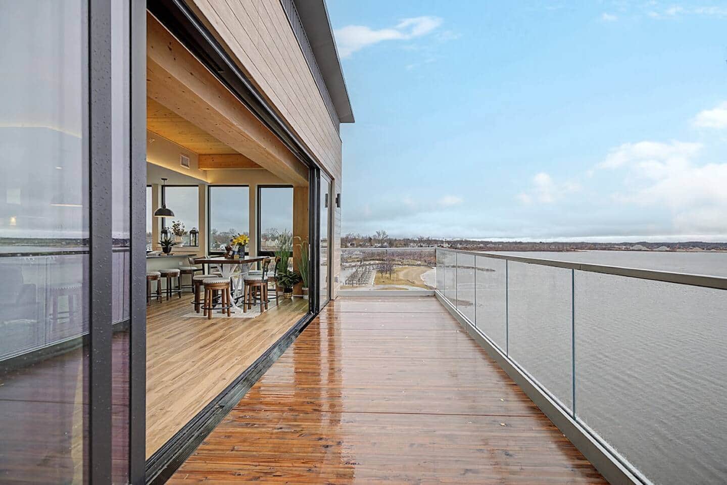 Private top-floor balcony at Above the Marina running along floor-to-ceiling glass walls, with Muskegon Lake and the Adelaide Pointe shoreline stretching out below