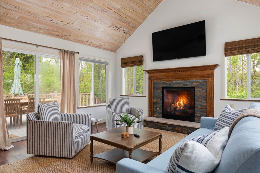 Bright living room with vaulted whitewashed-wood ceiling, stone fireplace, striped armchairs, and a soft blue sofa