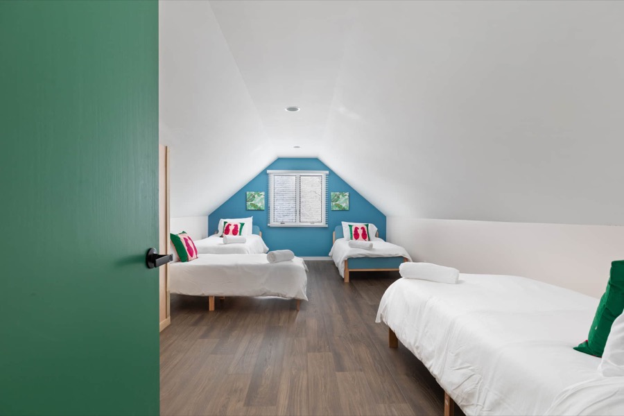 The bright vaulted bunk room: twin beds against a teal accent wall with a queen alongside — part of the four-bed kids' hangout