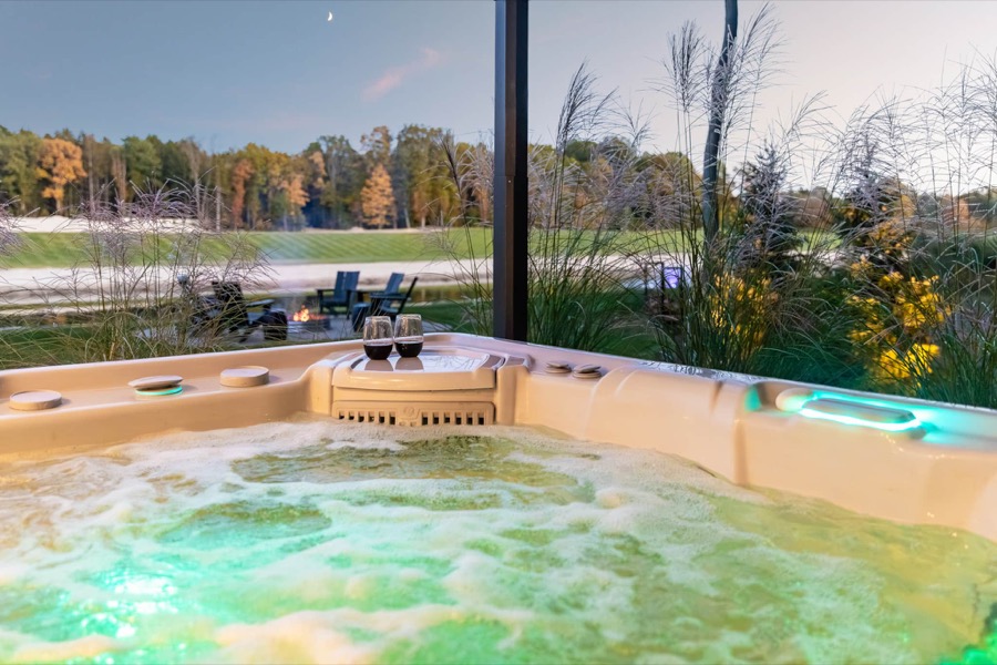 Hot tub with two glasses of wine on its ledge overlooking a calm private lake at dusk near Saugatuck