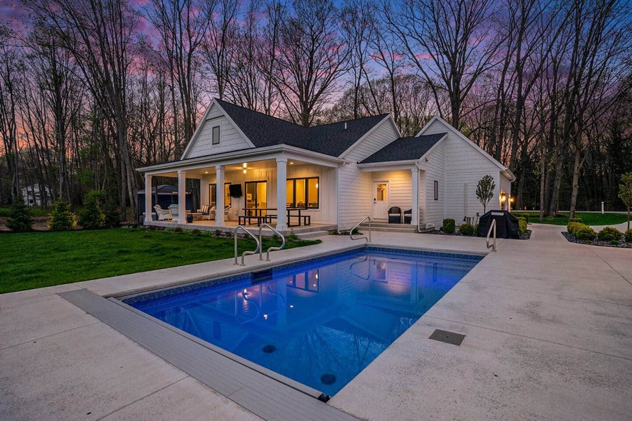 The heated pool glowing sapphire blue at dusk beside the covered back porch