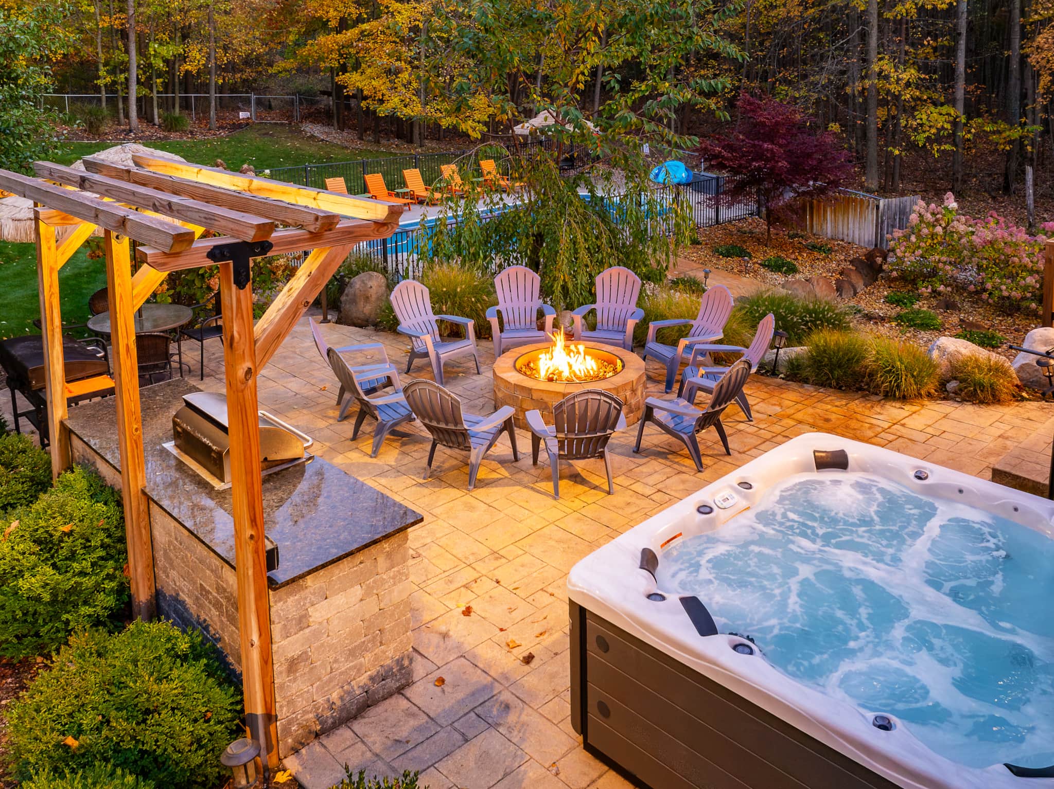 Autumn evening at Swimming in the Sunset in Fennville — Adirondack chairs circle a glowing fire pit beside a steaming hot tub, with the heated pool beyond