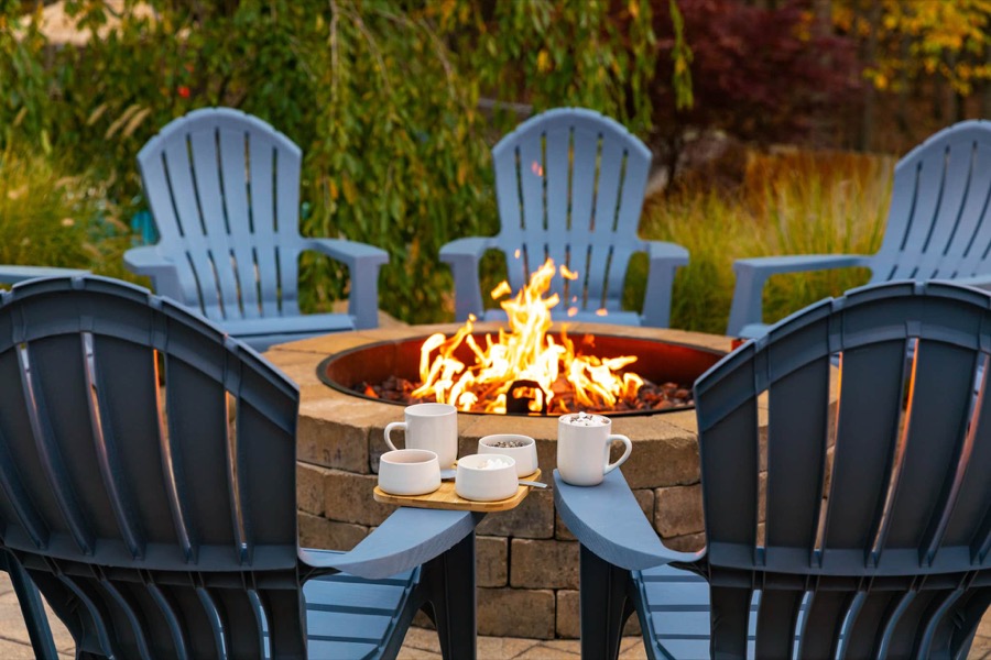 Mugs of cocoa and marshmallows on an Adirondack armrest beside the roaring stone fire pit