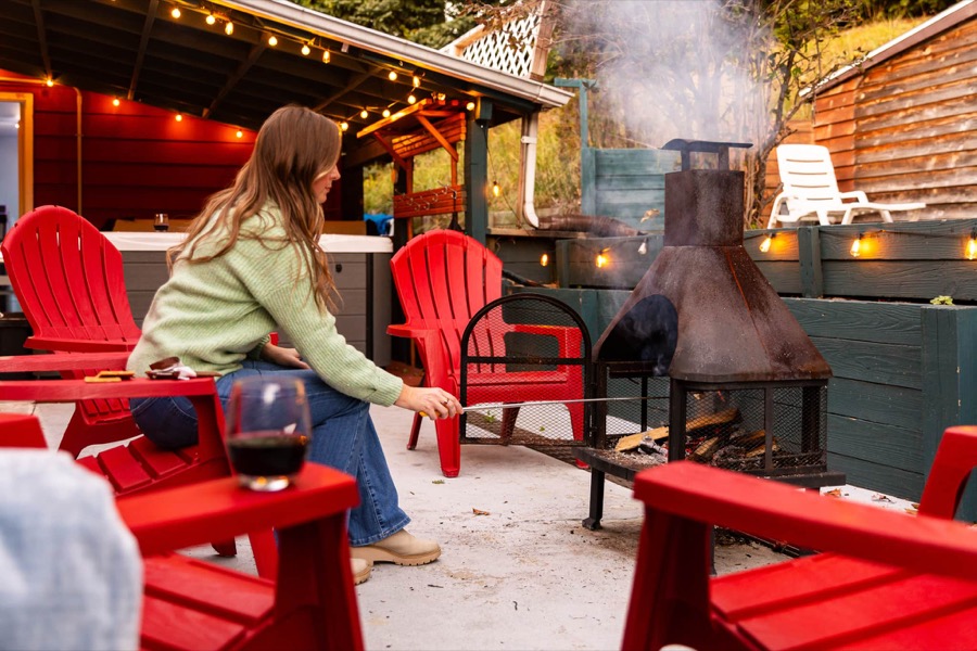 Roasting marshmallows over the chiminea fire pit from a circle of red Adirondack chairs, string lights and the hot tub behind
